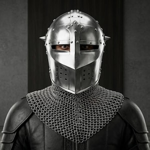 May include: A polished silver metal knight helmet with a central vertical ridge, horizontal eye slits, and small circular ventilation holes. The helmet is paired with a silver chainmail aventail that covers the neck and shoulders over black armor.