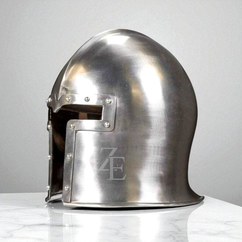 K&ouml;nnte beinhalten: Ein polierter silberfarbener Metallhelm mit abgerundeter Oberseite und rechteckiger Augen&ouml;ffnung. Nieten sichern das Visier. Der Helm hat die eingravierten Buchstaben "ZE" auf der Vorderseite. F&uuml;r historische Nachstellung oder Ausstellung.