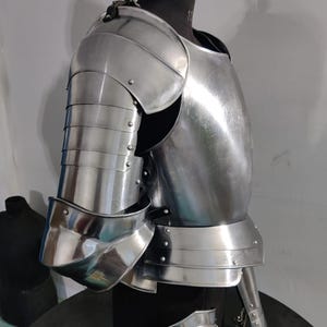May include: A polished steel suit of armor featuring a segmented shoulder pauldron, a curved breastplate, and articulated arm plating. The metallic components are joined with small rivets and leather straps, displaying a reflective silver finish.