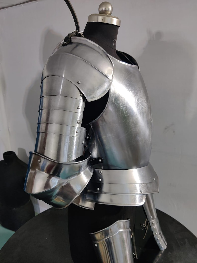 May include: A polished steel suit of armor featuring a segmented shoulder pauldron, a curved breastplate, and articulated arm plating. The metallic components are joined with small rivets and leather straps, displaying a reflective silver finish.