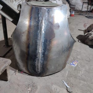 May include: A metallic chest plate featuring a central vertical ridge and a polished finish with visible heat-treated discoloration along the seam. The armor piece has a curved, contoured shape designed to protect the torso with a smooth surface.