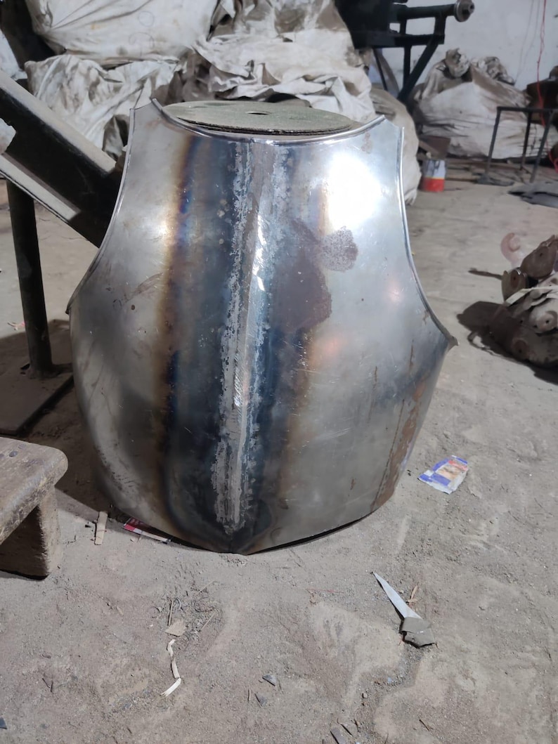 May include: A metallic chest plate featuring a central vertical ridge and a polished finish with visible heat-treated discoloration along the seam. The armor piece has a curved, contoured shape designed to protect the torso with a smooth surface.