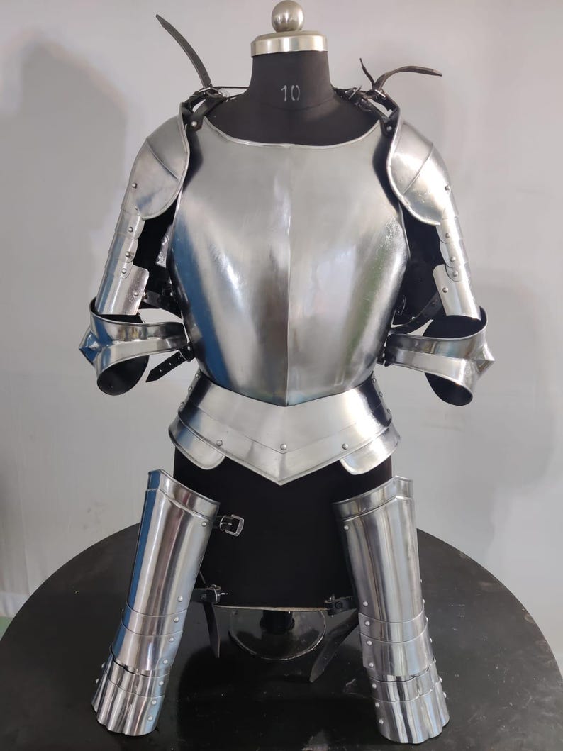 May include: A polished steel suit of armor displayed on a mannequin. The set includes a breastplate, shoulder pauldrons, arm guards, and leg greaves, all featuring a reflective metallic finish and secured with black leather straps and metal buckles.