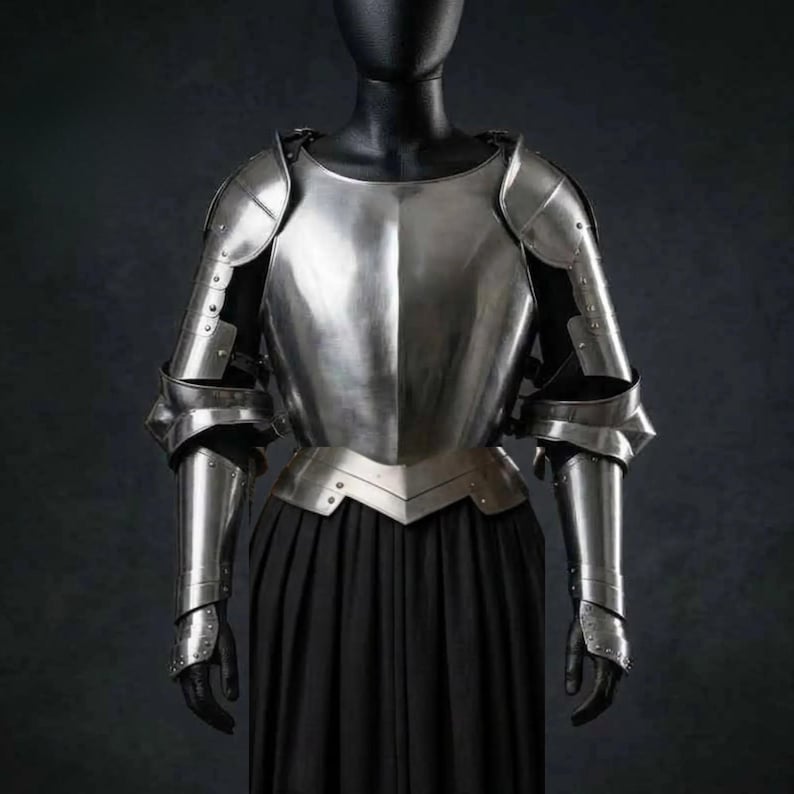 May include: A polished steel breastplate and pauldrons set featuring a central ridge on the chest, articulated shoulder guards, and matching arm defenses. The metallic armor pieces are displayed on a mannequin torso over a long black garment.