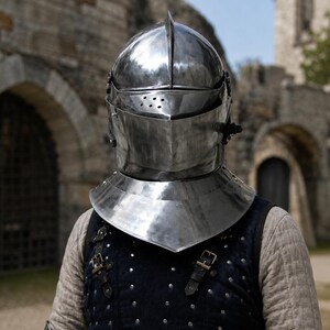 May include: A polished steel knight helmet featuring a rounded dome, a central ridge, and a visor with a series of small circular ventilation holes. The helmet includes a wide gorget neck guard and is worn over a dark quilted vest with metal buckles.
