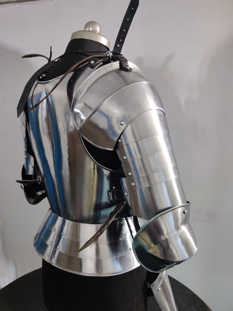 May include: A polished steel suit of armor torso piece featuring a breastplate, a segmented shoulder pauldron, and a full arm guard with a rounded elbow cop. The armor is secured with black leather straps and metal buckles over a dark mannequin.