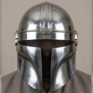 Puede incluir: Un brillante casco plateado de estilo Mandaloriano, con una distintiva visera en forma de T. El casco tiene un acabado met&aacute;lico liso y una prominente cresta central. El dise&ntilde;o incluye orejeras y una pantalla de malla.