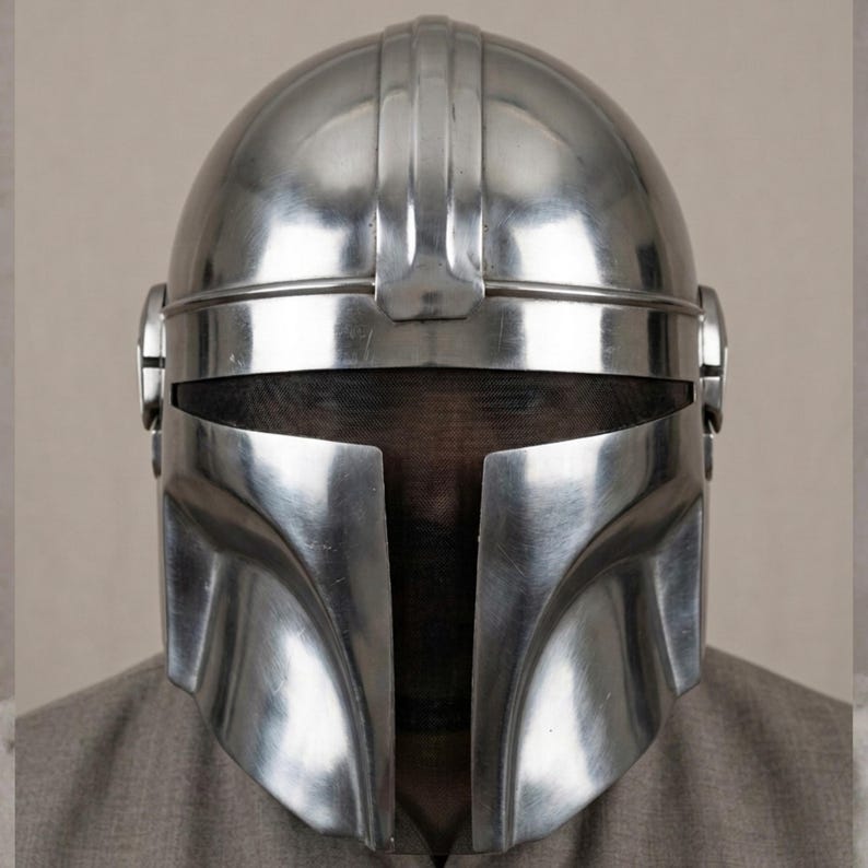 Puede incluir: Un brillante casco plateado de estilo Mandaloriano, con una distintiva visera en forma de T. El casco tiene un acabado met&aacute;lico liso y una prominente cresta central. El dise&ntilde;o incluye orejeras y una pantalla de malla.