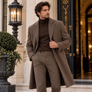 May include: A brown wool-blend overcoat worn over a dark brown turtleneck jumper and matching brown trousers. The overcoat features notched lapels, long sleeves, and a structured fit. The trousers are tailored with a clean, straight-leg silhouette.