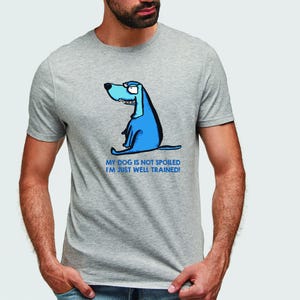 Op de afbeelding: Lichtgrijs t-shirt met een blauwe cartoonhond en de tekst "MY DOG IS NOT SPOILED I'M JUST WELL TRAINED!". De hond heeft een zelfvoldane uitdrukking. Het t-shirt heeft korte mouwen.