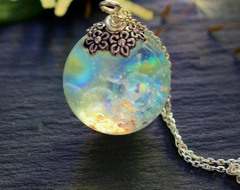 May include: A round, iridescent pendant necklace with a silver chain. The pendant is a clear orb filled with colorful glitter and a decorative silver cap. The necklace is a piece of jewelry.