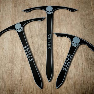 Puede incluir: Tres herramientas negras en forma de T con gráficos de calaveras grises y bordes blancos. Cada herramienta incluye texto que indica su longitud: 8 inches, 9 inches y 6 inches. Las herramientas tienen un extremo inferior puntiagudo y una barra superior curva.