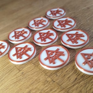 Pode incluir: Dez fichas de jogo circulares em branco e cobre. Cada ficha tem um centro branco com um desenho geométrico acobreado e uma borda acobreada. As fichas estão dispostas sobre uma superfície de madeira.