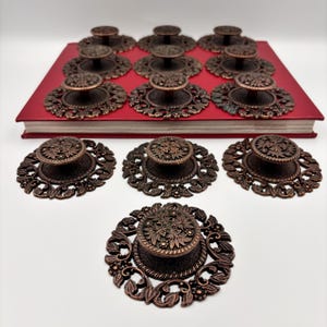 May include: Bronze-coloured cabinet knobs with floral designs. The knobs are arranged on a red surface, with some displayed separately. The knobs have a vintage, antique aesthetic, suitable for furniture restoration.