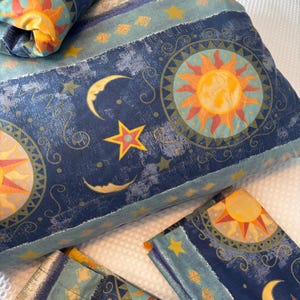 May include: A celestial-themed pillow and pillowcases set. The navy blue fabric features a sun, moon, and star design in shades of yellow, orange, and gold. The set includes a pillow and two pillowcases, perfect for a bedroom.