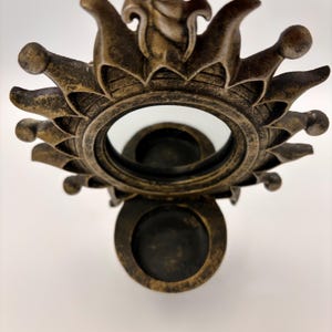 May include: A wall-mounted candle holder featuring a circular mirror framed by a sunburst design with pointed rays. The frame has a distressed bronze finish and includes a small, circular platform at the base for holding a single candle.