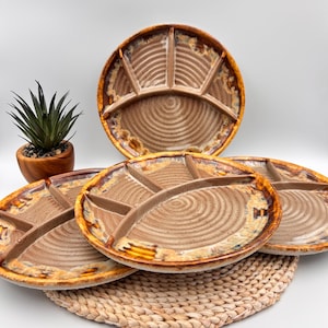Peut inclure: Ensemble de quatre plateaux de service divisés en céramique marron et beige avec un motif en spirale. Les plateaux ont un aspect rustique et artisanal avec une finition émaillée et sont disposés sur un dessous de plat tressé. Une petite plante en pot est en arrière-plan.