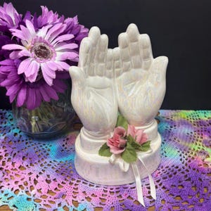 May include: A white ceramic mug with a black handle and the text "But First, Coffee" in a bold, black font. The mug is set against a blurred background. The mug is approximately 10 cm tall.