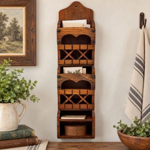 May include: A vertical wall-mounted wooden organiser featuring three distinct storage tiers. The unit is crafted from dark stained wood and includes a top section for mail, a middle section with a lattice design, and a bottom shelf for small items.