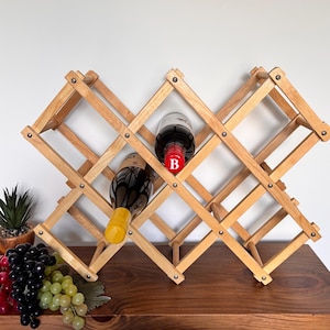 Peut inclure: Un casier à vin en bois avec un motif en treillis de losanges, contenant deux bouteilles de vin. Le casier est en bois clair et a un design pliable et extensible. Les bouteilles sont remplies de vin rouge.