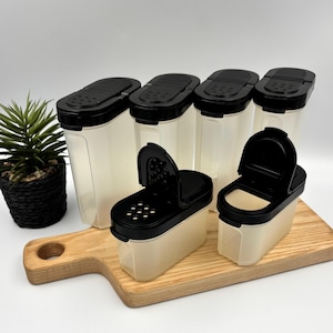 Peut inclure: Un ensemble de six récipients à épices en plastique translucide avec des couvercles noirs, comprenant quatre grands contenants rectangulaires et deux plus petits avec des couvercles à charnière. Les couvercles ont des trous perforés.