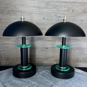 Könnte beinhalten: Zwei passende schwarze Tischlampen mit einem kuppelförmigen Schirm und einer silbernen Spitze. Die Lampen haben einen zylindrischen schwarzen Sockel mit türkisfarbenem Akzent und einen kreisförmigen Sockel. Die Lampen sind etwa 46 cm hoch.