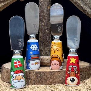 Juego de 4 cuchillos para untar navideños, con mangos de cerámica decorados con Papá Noel, renos y muñecos de nieve, en una caja de regalo vintage.