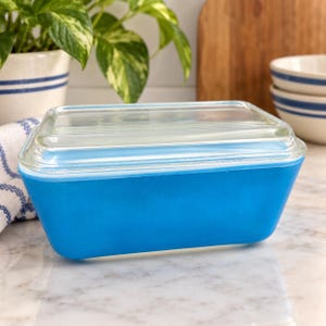Peut inclure: Un récipient de stockage rectangulaire en verre bleu vif avec un couvercle en verre transparent. Le récipient présente une base bleue opaque et solide avec une finition lisse et un couvercle transparent légèrement nervuré qui s'ajuste.