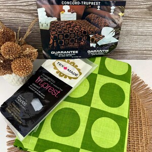 Peut inclure: Une présentation à plat d'une parure de lit Concord-Truprest vintage. L'image comprend un drap à motifs verts et blancs, un drap emballé avec le logo Truprest et une brochure. La brochure annonce une parure de lit avec un motif géométrique marron et noir.