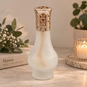 May include: A fragrance lamp with a frosted glass base featuring a subtle embossed wheat pattern and a metallic gold-toned crown top with a decorative cut-out design. The lamp has a rounded body that tapers towards the neck and a flared base.