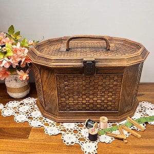 Peut inclure: Une boîte à couture vintage en bois avec un motif tissé et une poignée. La boîte est marron et possède un fermoir en métal. La boîte est sur une table en bois avec de la dentelle et des fournitures de couture.