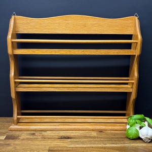 May include: A light brown wooden spice rack with four shelves. The rack has a curved top and is designed to be mounted on a wall. The rack is empty, ready to be filled with spices. The rack is made of wood and has a natural finish.