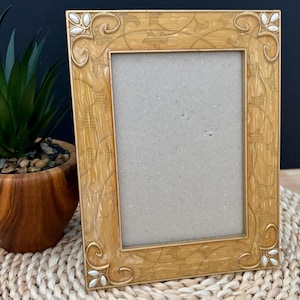 May include: A rectangular picture frame with a glossy, marbled golden-yellow finish. The frame features an embossed, swirling vine pattern across its surface and small, white, teardrop-shaped accents at each of the four rounded corners.