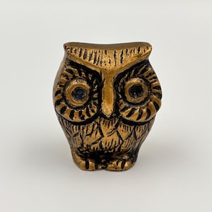 May include: A bronze owl figurine with detailed carvings. The owl has large, round eyes with blue accents and a textured finish. This decorative item is likely for display, suitable for home decor or as a collector's item.