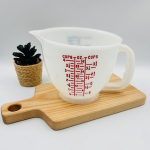 Peut inclure: Un pichet doseur en verre opalin blanc avec une anse et un bec verseur. L'extérieur présente des graduations imprimées en rouge indiquant des mesures en tasses et en onces, allant de 4 tasses et 32 onces à 1/2 tasse et 4 onces.