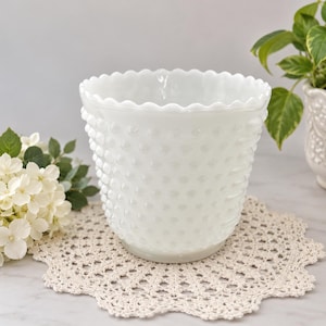 Puede incluir: Una maceta de vidrio lechoso blanco con una textura de relieve tipo hobnail en toda la superficie exterior. El recipiente tiene una abertura circular ancha con un borde festoneado. El vidrio es opaco y liso, mostrando un patrón repetido de pequeños bultos.