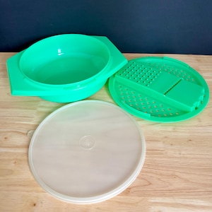 Puede incluir: Un juego de vaporera de plástico verde con un cuenco, un inserto de rallador perforado y una tapa transparente. El cuenco tiene asas. El inserto del rallador tiene un borde dentado. La tapa es redonda.