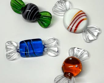 Könnte beinhalten: Vier farbenfrohe Glas-Bonbon-Skulpturen. Eine ist schwarz und grau, mit grünen Wicklern. Eine andere ist weiß mit roten und orangen Streifen. Eine dritte ist blau mit schwarzen Streifen, und die letzte ist orange mit weißen Punkten.