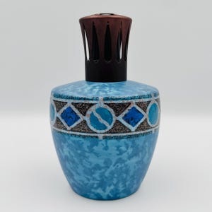 May include: A blue fragrance lamp with a mottled finish and a decorative band featuring alternating dark blue diamonds and circles. The lamp is topped with a dark brown metal crown-shaped burner cap that has vertical cutouts for ventilation.