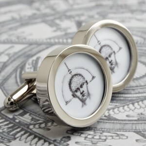 May include: A pair of silver cufflinks with a circular design. Each cufflink features a black and white illustration of a human head with a diagram of the brain. The cufflinks have a polished, reflective finish.