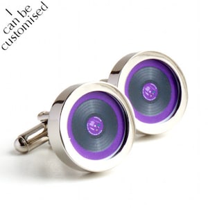 May include: A pair of silver cufflinks with a purple and black vinyl record design. The cufflinks have a circular face with a silver border and a T-bar closure. The text "I can be customized" is in the upper left corner.