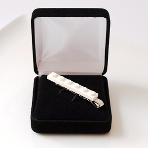 May include: A white Lego tie clip in a black velvet box. The tie clip is made of five Lego bricks.