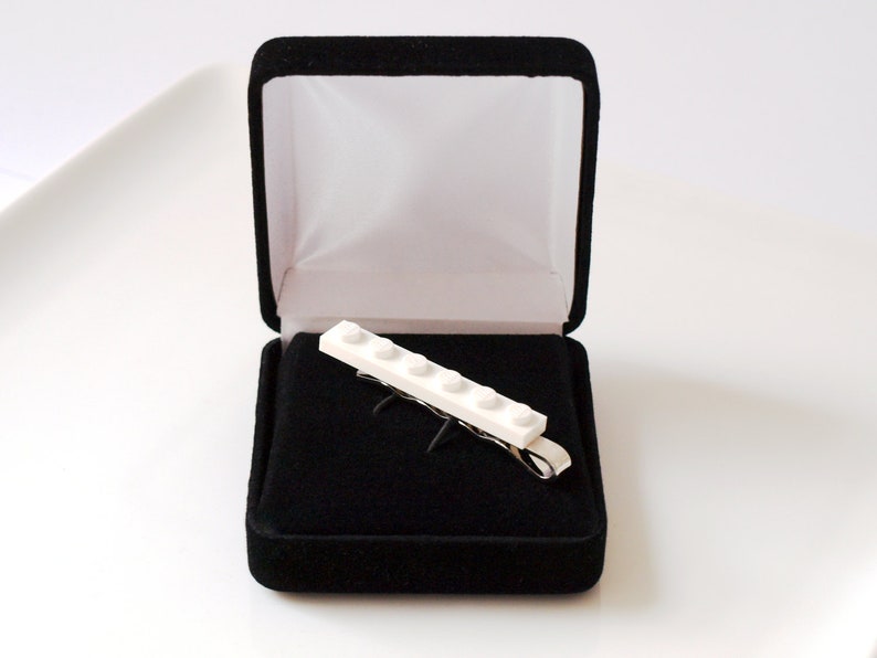 May include: A white Lego tie clip in a black velvet box. The tie clip is made of five Lego bricks.
