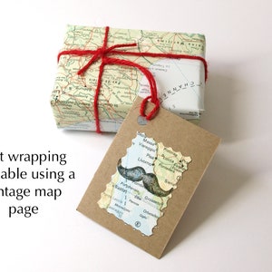 May include: A gift wrapped in a vintage map page, tied with red twine. A tag cut in the shape of a map with a mustache graphic is attached. The text "Gift wrapping available using a vintage map page" is visible.