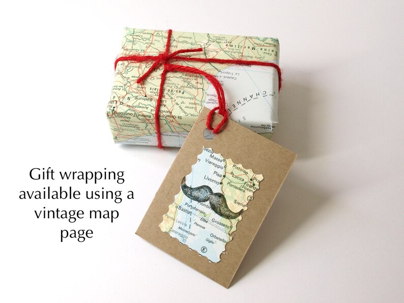 May include: A gift wrapped in a vintage map page, tied with red twine. A tag cut in the shape of a map with a mustache graphic is attached. The text "Gift wrapping available using a vintage map page" is visible.