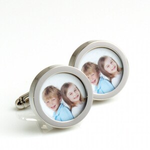 May include: Silver-toned cufflinks with a circular design. Each cufflink features a photograph of two smiling children. The photos are framed by a polished silver border, creating a personalized accessory.