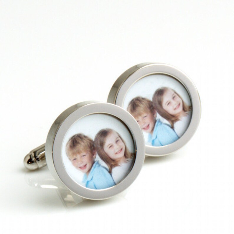 May include: Silver-toned cufflinks with a circular design. Each cufflink features a photograph of two smiling children. The photos are framed by a polished silver border, creating a personalized accessory.