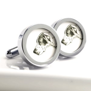 May include: A pair of silver cufflinks with a black and white illustration of a dog's head on each cufflink.