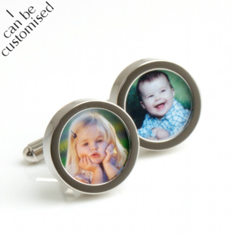 May include: A pair of silver cufflinks, each featuring a circular design with a photo of a child. One cufflink shows a smiling baby in a blue plaid shirt, and the other shows a young girl. The text "I can be customized" is in the upper left corner.