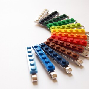 May include: A set of 12 colorful hair clips made from LEGO bricks. The clips are arranged in a rainbow pattern, with each clip featuring a different color.